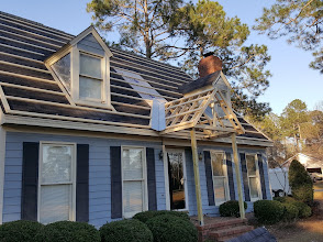 New wooden gable portico being framed over the front entry of a blue house with dark shutters
